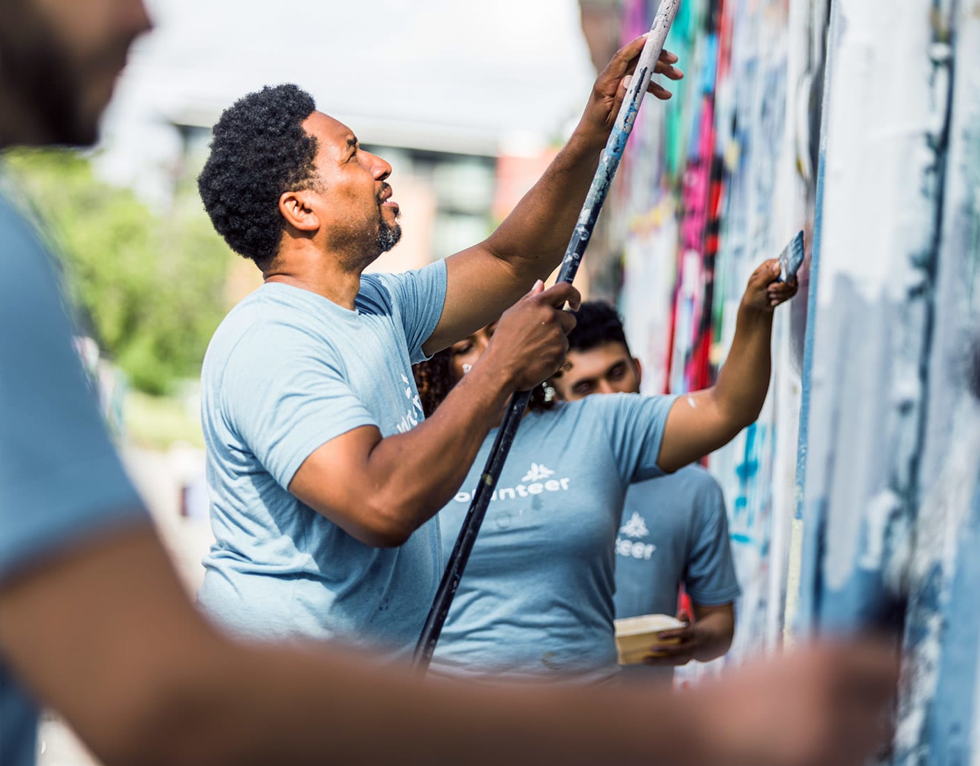 A diverse group of volunteers in matching t-shirts collaboratively painting a large wall with bright colors and paintbrushes.